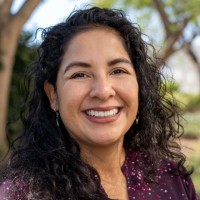 Photo of Marcela Reyes, a smiling woman with brown eyes and brown hair. She is posing outside with a background of trees.