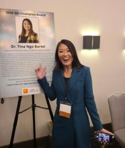 Dr. Tina Ngo Bartel smiles while pointing to a display board with her photo and bio.